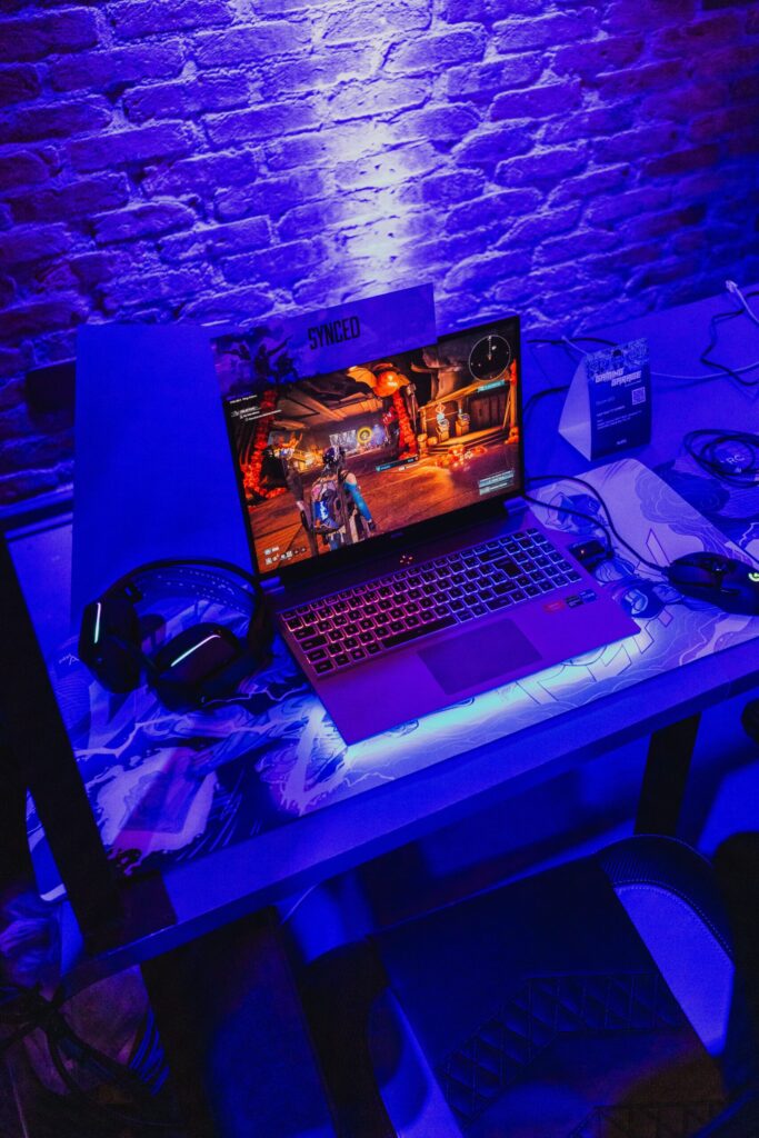 Moderne Gaming-Laptop mit Kopfhörern und Maus auf dem Schreibtisch in lila Neonbeleuchtung.